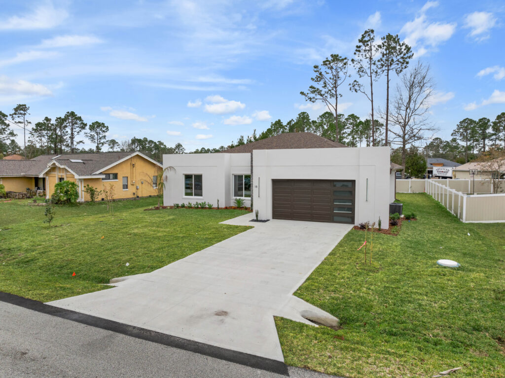 New white stucco single-story home with brown garage door, concrete driveway and fresh sod in Palm Coast