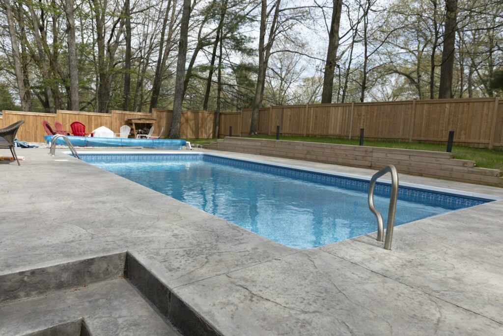 Rectangular in-ground pool with a concrete deck, steel handrails and a wood privacy fence around the backyard